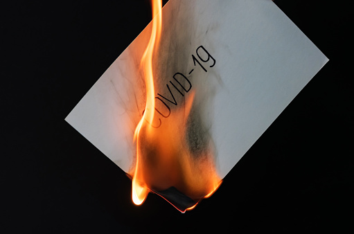 Burning sheet of paper with the text COVID-19 on a black background.