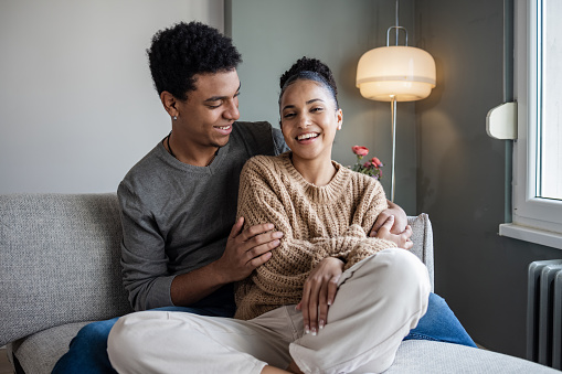 Portrait of African American couple in love sitting comfortable on the couch in the living room. They are spending their free time together. Weekend activities.