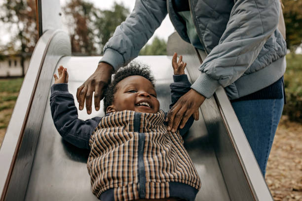 Love to play Mother and son have fun playing in  playground. Boy is going down the slide sliding down stock pictures, royalty-free photos & images