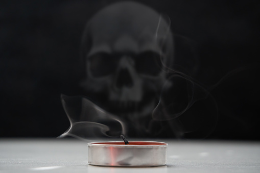 An extinguished candle with a wick from which smoke is coming. In the background is a skull. Soft selective selective focus.