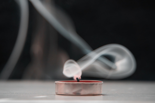 A extinguished candle emitting smoke standing on the table, a black background. Soft selective focus.