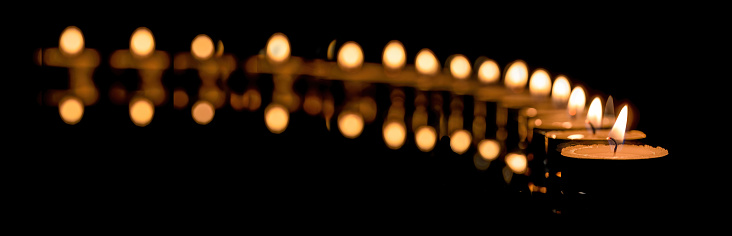 a row of candles burn in the dark. The flame of burning candles on a dark background.