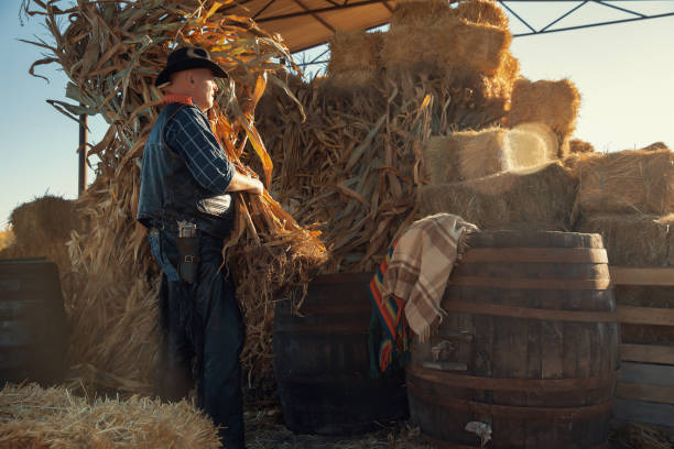 istock Hardworking farmer in a blue jacket and cowboy hat cleans up hay bales 1437280014