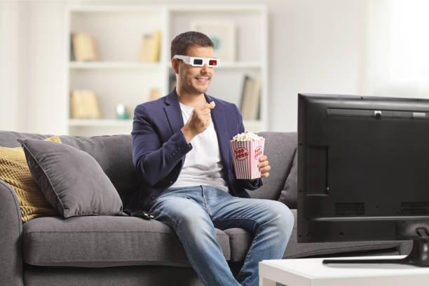 istock Man with 3d glasses eating popcorn and sitting on a sofa at home 1437281341