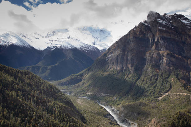 Hikers are seen trekking toward Annapurna Base Camp in Nepal. The trail winds through a snowy landscape in the Himalayas mountains, beneath a bright blue sky.