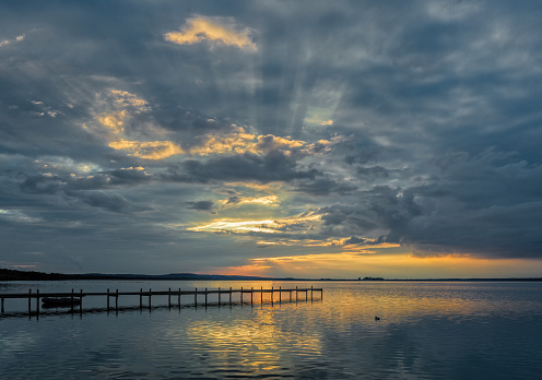 Sunbeams and majestic cloudscape  over jetty on lake at sunset