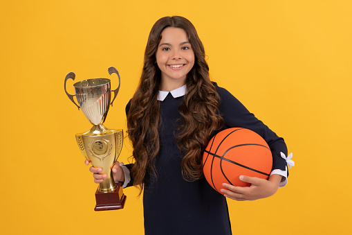 glad child hold basketball ball and champion cup on yellow background, victory.