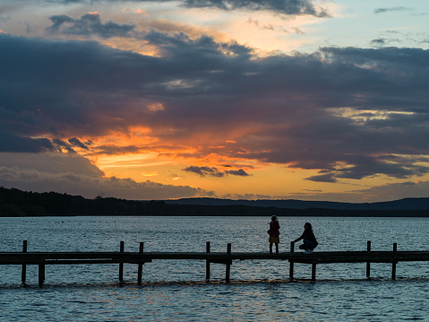 Silhouette of mother and daughter on jetty with afterglow over lake at dusk