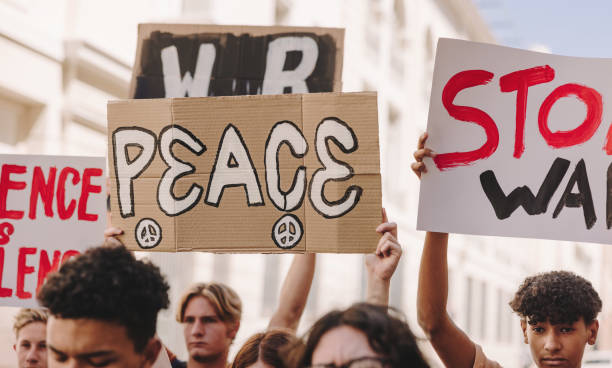 Young people marching against war and violence in the city Multicultural young people marching the streets for world peace. Teenage activists raising banners and placards during an anti-war rally in the city. Demonstrators protesting against war and violence. peace demonstration stock pictures, royalty-free photos & images