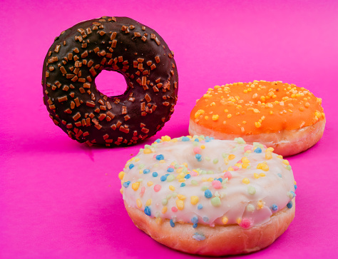 Sweet tasty doughnut with sprinkles on pink background