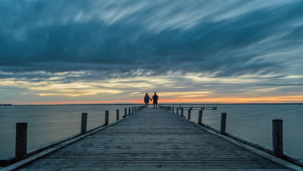 coppia che tiene le mani in piedi sul molo al crepuscolo con bagliore sul lago - steinhuder meer foto e immagini stock