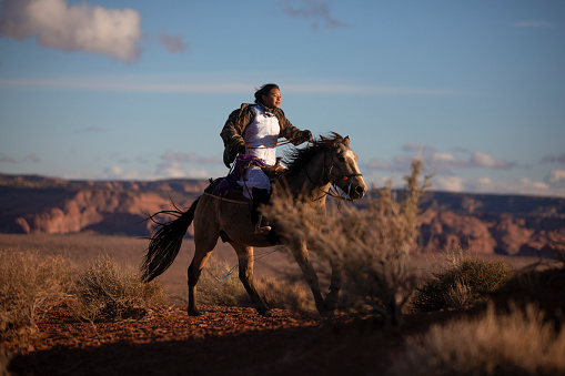 Navajo native american girl on horse running fast In the Arizonas desert at sunset