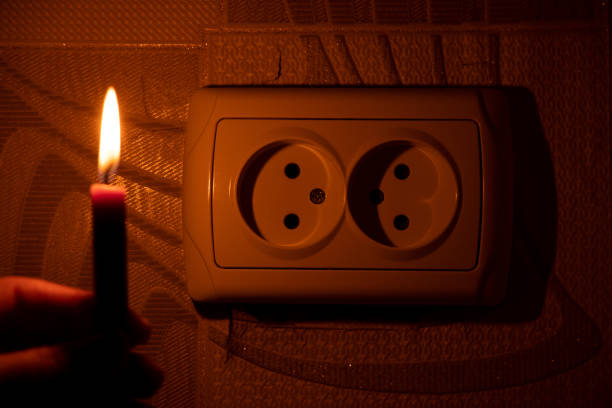 Female hand with a candle near the socket on the wall in the apartment in the dark, Ukraine, lack of light due to the war, power outages 2022 stock photo