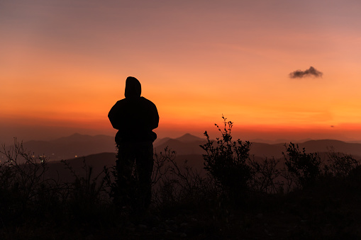 The red sunset glow fills the sky at dusk, and a person's back on the mountain