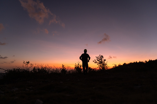 The silhouette of a person walking on the top of the mountain at dusk, facing the red sky and sunset