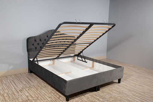 A gray bed with a storage space revealed by lifting the wooden slatted base