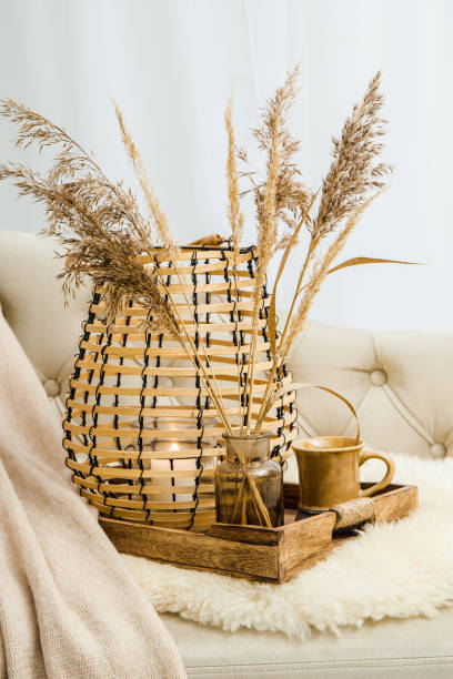 Cozycore or cottagecore concept, warm soft brown beige interior design objects. Cozy wool plaid on sofa, candle burning in wood lantern, tea cup on wood serving tray. Warm color photo manipulation. concepto cozycore o cottagecore, cálidos objetos de diseño de interiores de color beige marrón suave. acogedora lana a cuadros en el sofá, vela encendida en linterna de madera, taza de té en bandeja de servir de madera. manipulación de fotos en color