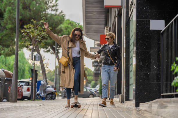 Two adult women learn to ride skateboard in a city. Urban lifestyle scene in Barcelona. stock photo