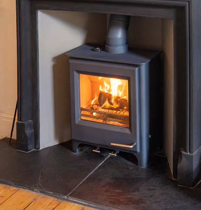 Logs burning in a modern wood burning stove to warm a room during winter, with a metal mantlepiece surround on a slate base.