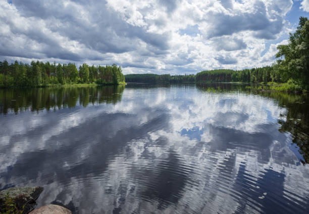Landscape with white and grey clouds reflecting in calm lake in Repovesi National park on beautiful summer day.