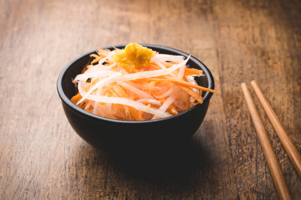 namasu japanischer daikon- und karottensalat oder kohaku (rot und weiß) salat mariniert in reisessig serviert mit zitronenschale. warmer holzhintergrund. vegetarische rezepte yasai, neujahrsfeier, nahaufnahme - yasai stock-fotos und bilder