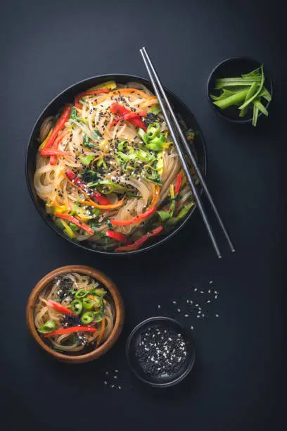 Korean style instant noodle Japchae or Chapchae. Stir-fried Korean vermicelli noodles with vegetables topped with white and black sesame. Korean traditional food style still life