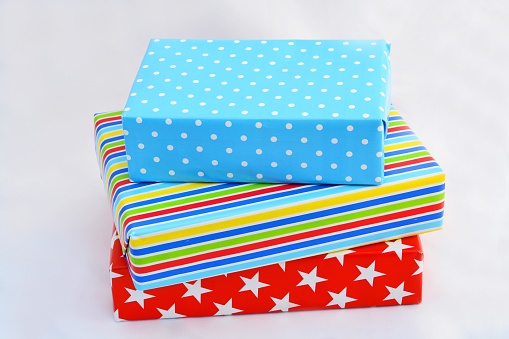 An isolated closeup shot of gift boxes in colorful wrapping stacked on top of  each on white background