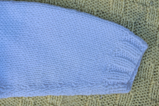 one sleeve of a woolen sweater lies on a green knitted fabric of clothing