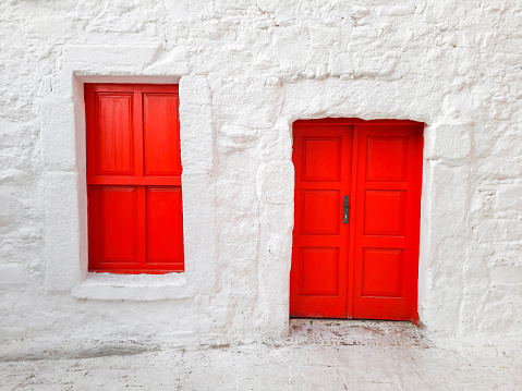 Door and window with closed shutters of red color in a house with white walls, Turkish building, national colors.
