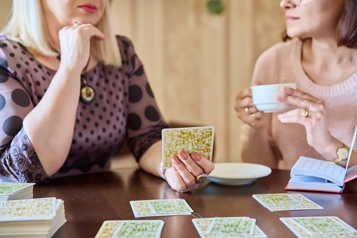 Two middle aged women laying out cards at home on the table. Game, psychology, metaphorical associative cards, esotericism prediction, communication lifestyle friendship of mature women