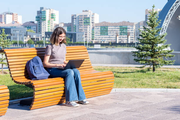 A Spanish student girl with glasses typing text on a laptop, looking for something on the Internet, chatting online with friends