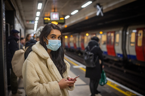 Young Indian girl in London waits for her tube while messaging on cell phone.