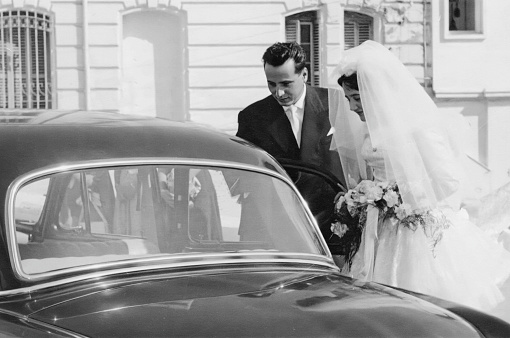 Vintage image from the 50s: Young couple walking from the church into a car after getting married