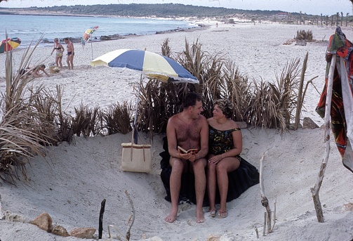 Catalonia (unfortunately unknown), Spain, 1965. Holidaymakers couple in their sand castle on a Spanish beach.