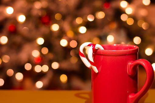Red mug with candy canes in front of defocused Christmas lights with copy space