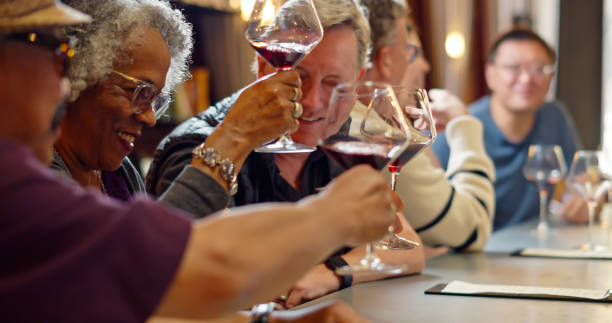 Friends Raising Wine Glasses for a Toast A diverse group of people sitting at the bar in a wine tasting lounge, drinking and chatting. wine bar counter stock pictures, royalty-free photos & images