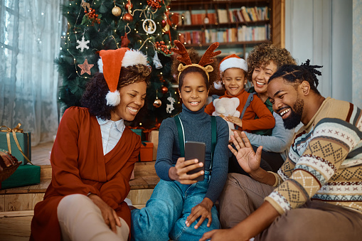 Happy African American girl and her extended family using smart phone while making video call on Christmas day.