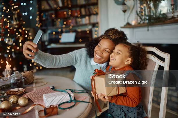 Cheerful Black Mother And Daughter Taking Selfie On Christmas Day At Home Stock Photo - Download Image Now