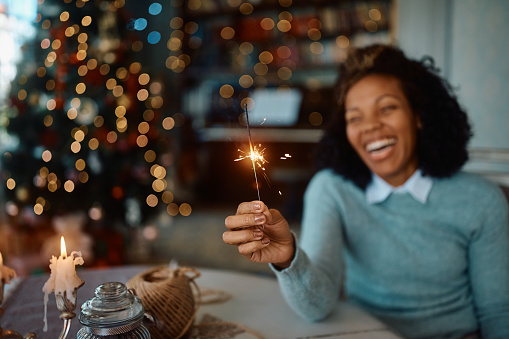 Close up of African American woman having fun while using sparkler during Christmas at home.
