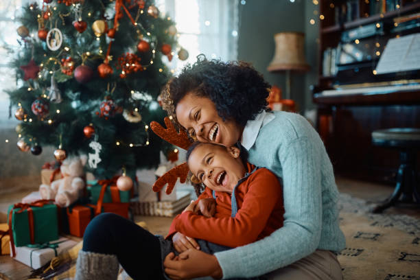 Cheerful African American mother and daughter having fun on Christmas day at home. stock photo