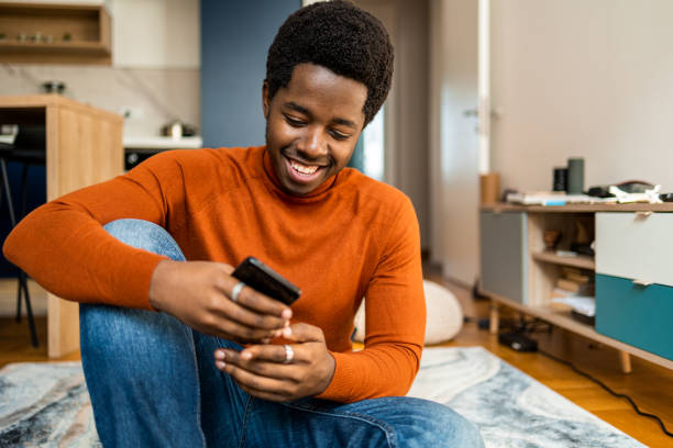 Smiling African American man relaxing at home with mobile phone stock photo