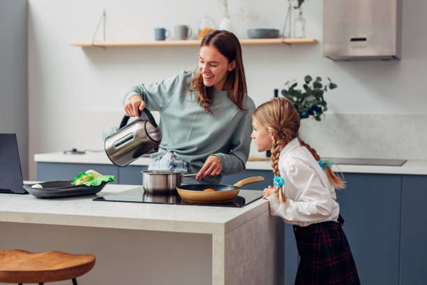 mujer cocina una comida con su curiosa hija colegiala cerca - stereotypical housewife little girls family domestic kitchen fotografías e imágenes de stock
