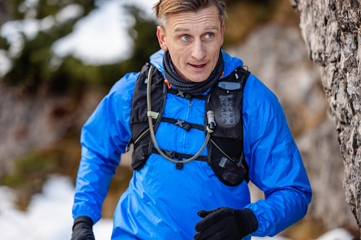 Front view shot of a Caucasian mature man in his 50's bounds up mountain trail in winter.