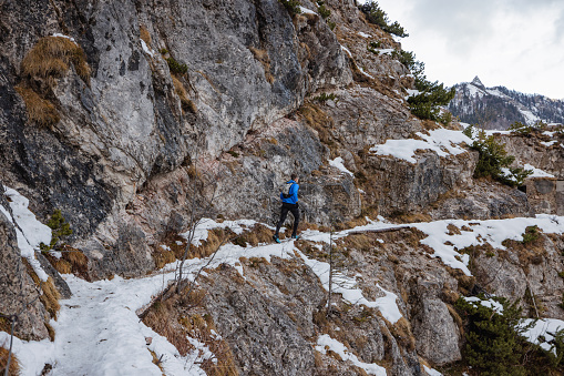 A rear view shot of a Caucasian active trail runner in his 50's, wearing sport clothes, running on mountain road alone in winter.