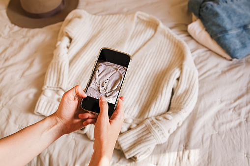 Close-up of woman's hands taking picture of her used sweater. Selling used clothes online, reuse, sustainable consumption