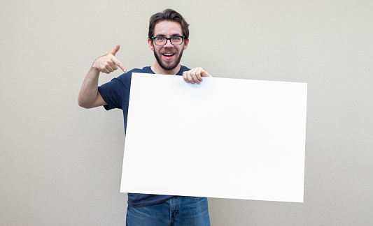 young guy pointing his finger to a big blank board poster for advertising promos