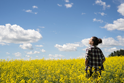 A young woman standing in a field of canola looking up with her eyes closed as she enjoys the warmth of the sun