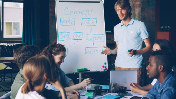 istock Creative manager is using whiteboard at business meeting pointing at chart and talking while group of people is listening and learning new information. 1437411423