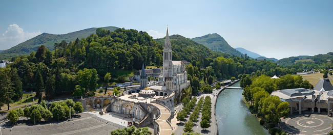 Famous Sanctuary of Our lady of Lourdes - Rosary Basilica Drone XXL Panorama - World famous Pilgrim destination. Cathedral of Lourdes,  Grotte de Massabille next to river Gave de Pau. Lourdes is a small market town lying in the foothills of the Pyrenees, famous for the Maria apparitions of Our Lady of Lourdes that are reported to have occurred in 1858 to Bernadette Soubirous. Our Lady of Lourdes Basilica in Lourdes, Lourdes,  Hautes-Pyrenees, France, Europe