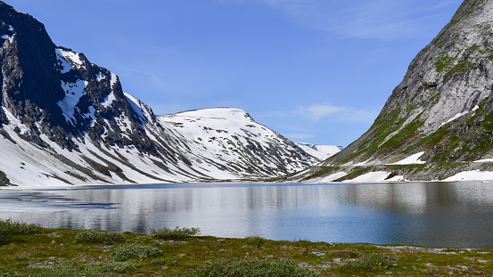 Fjord lake in snow capped mountain landscape, travel Norway on bright summer day, Scandinavia, Europe